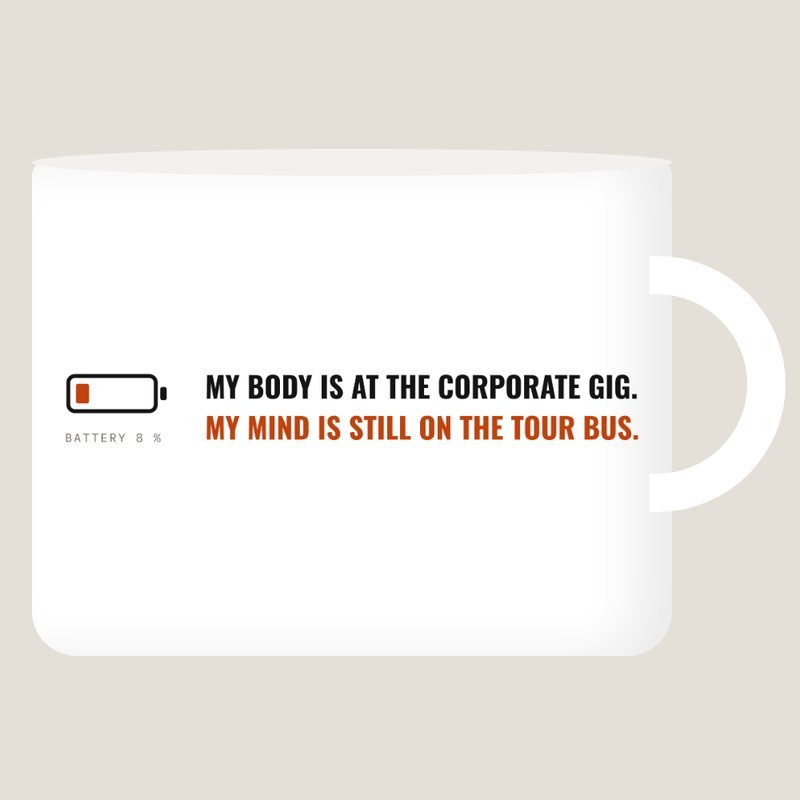 White mug with the saying: My body is at the corporate gig. My mind is still on the tour bus.